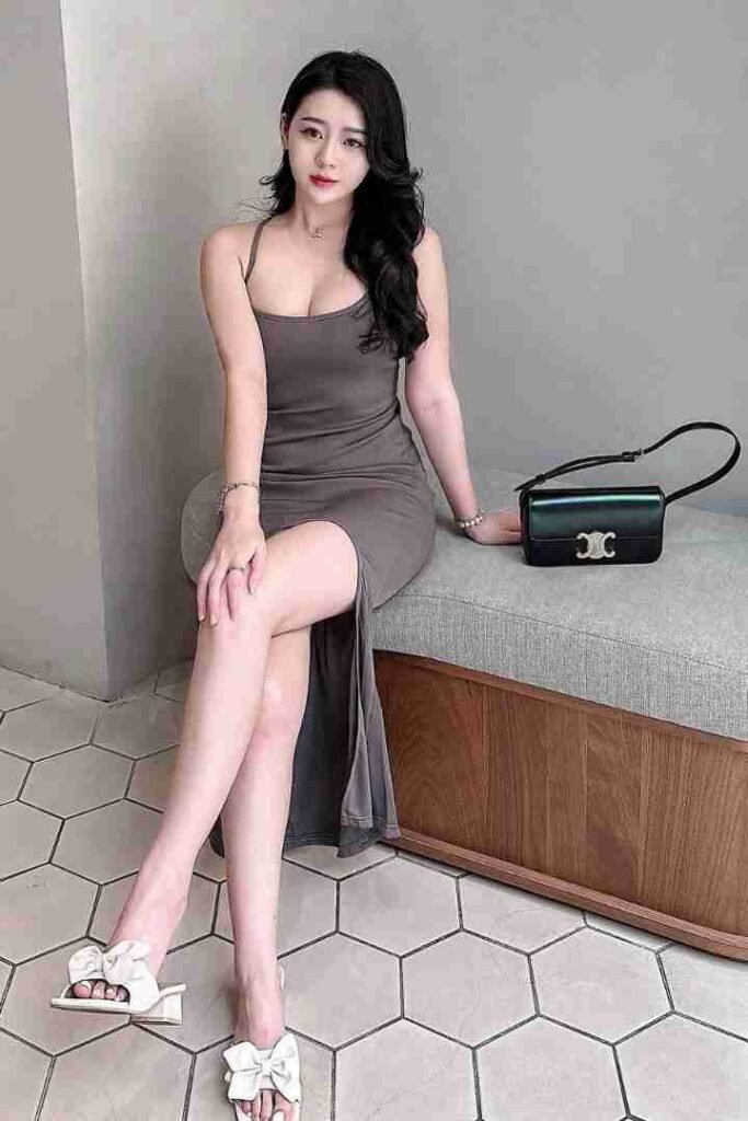 Malaysia Escort Girl Woman in gray dress with slit, black purse, and white sandals posing on a bench. Sex Service Kuala Lumpur