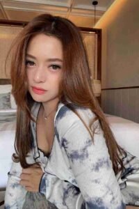 Malaysia Escort Girl Woman with long brown hair wearing a tie-dye top, posing indoors. Sex Service Kuala Lumpur