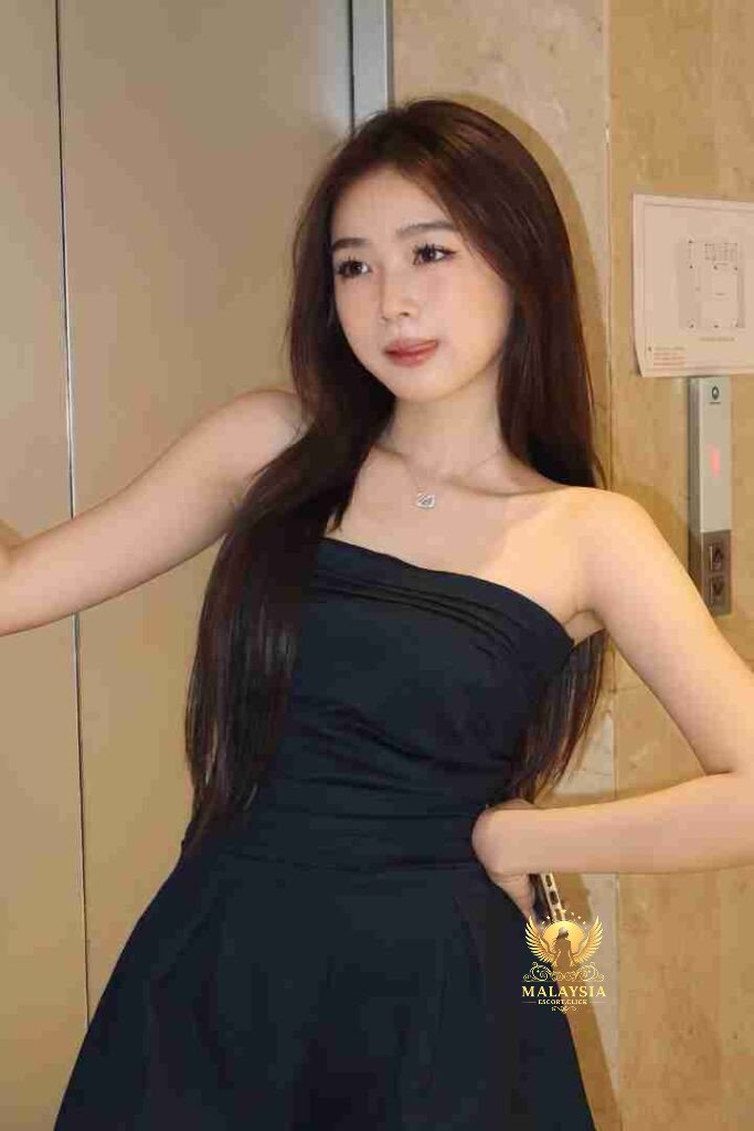Beautiful Asian woman in black strapless dress with long brown hair posing indoors.