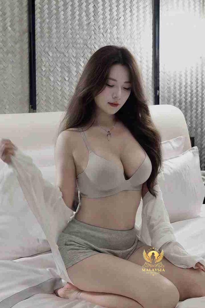 Asian woman in bra and shorts sitting on bed