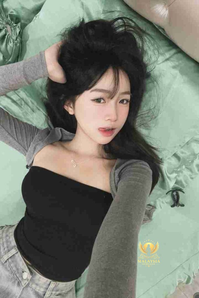 Asian woman lying on bed with black top and grey cardigan, looking at camera.