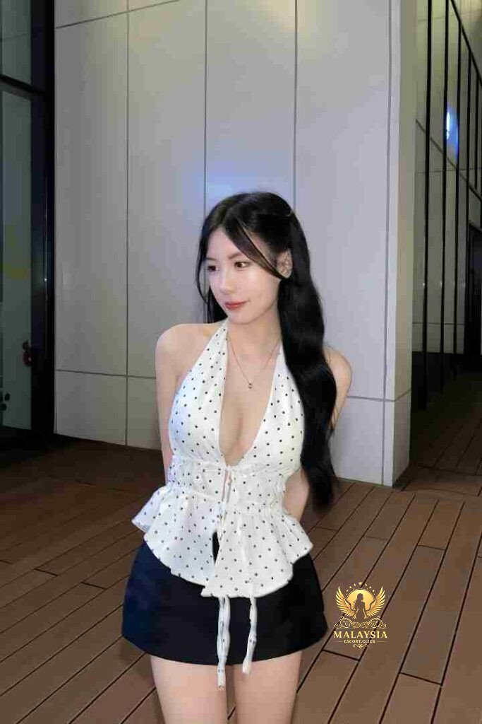 Attractive Asian woman in polka dot halter top and black shorts posing outdoors in urban setting.