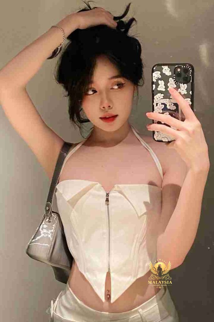 Woman in white corset top takes selfie. Fashionable Asian woman with dark hair and a stylish phone case.