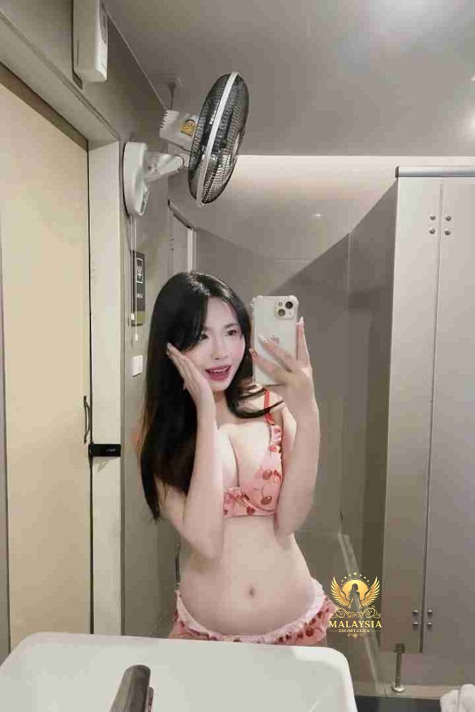 Woman in cherry print lingerie takes mirror selfie in bathroom with fan and white cabinets.