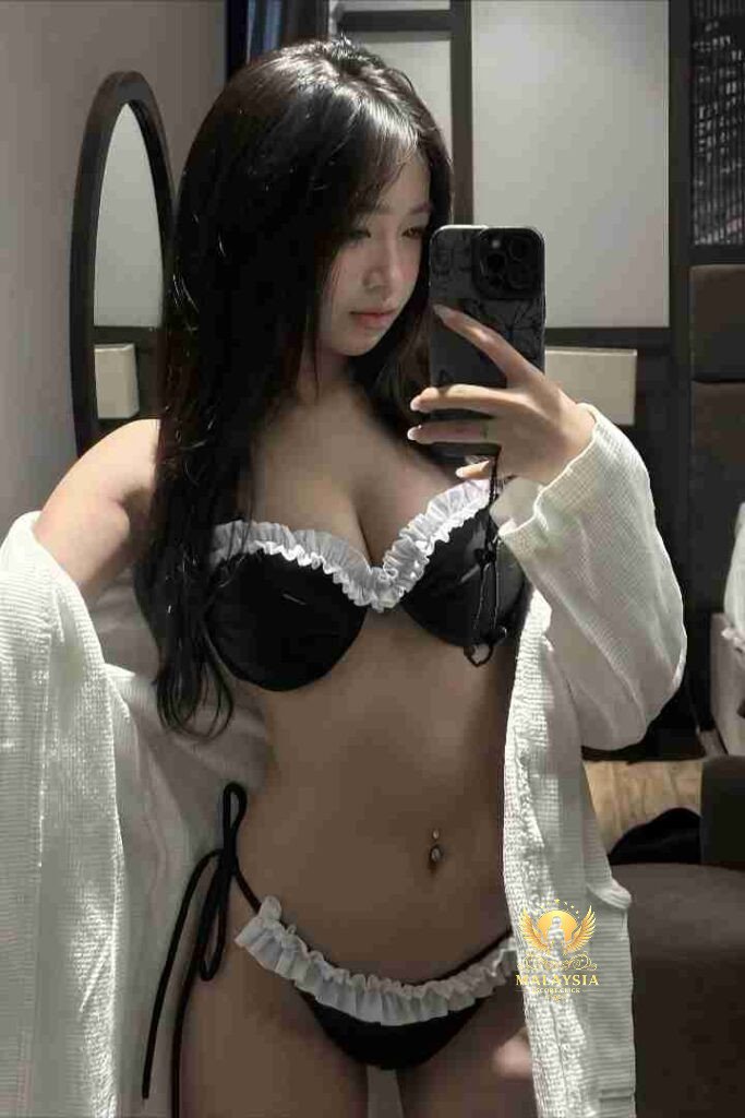 Woman in black and white lingerie taking a selfie in a bathroom mirror with white robe.