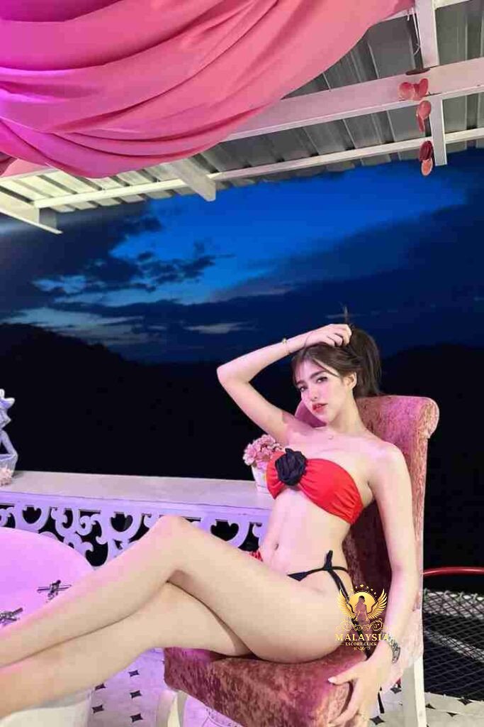 Woman in red bikini top sitting on chair outdoors at night with mountain view.