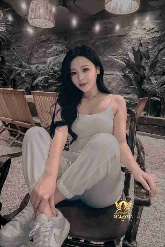 Woman in white outfit sitting on chair, posing indoors with plants and lights in background.